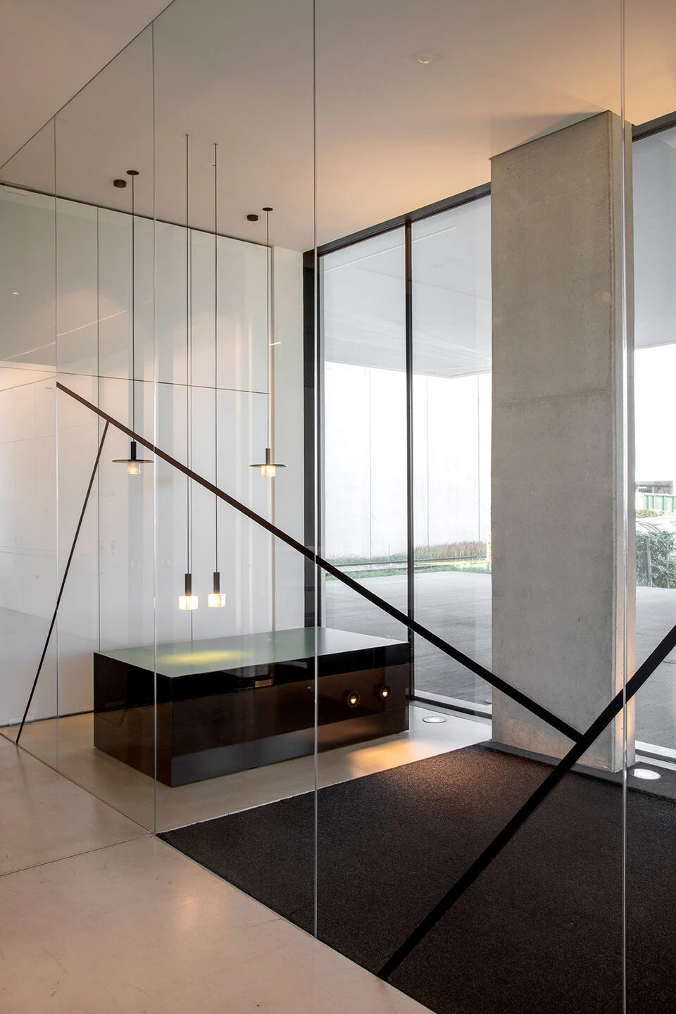 Clérachic Alabaster Pendant Lights hung in a row over a dark reception desk in a glass and concrete lobby.