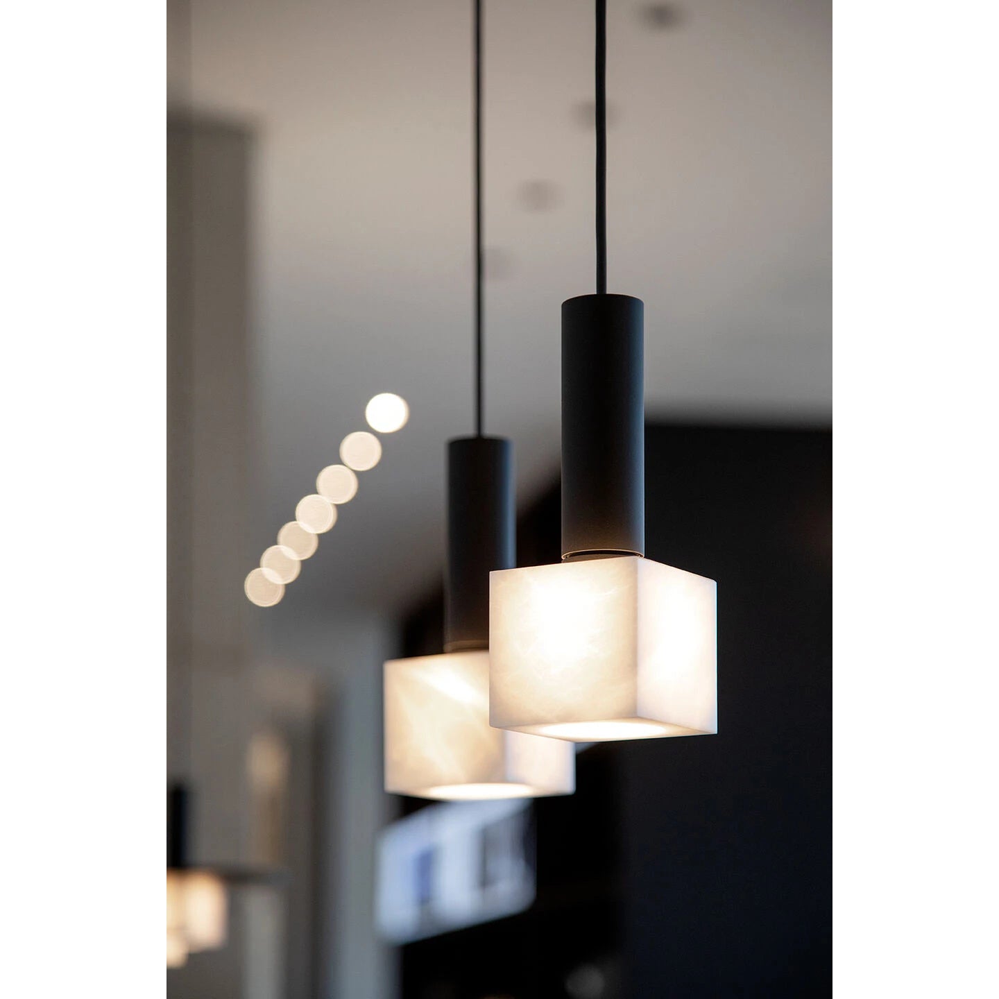 Two Clérachic Alabaster Pendant Lights at close range, warm light pooling through the square stone and out the open base.