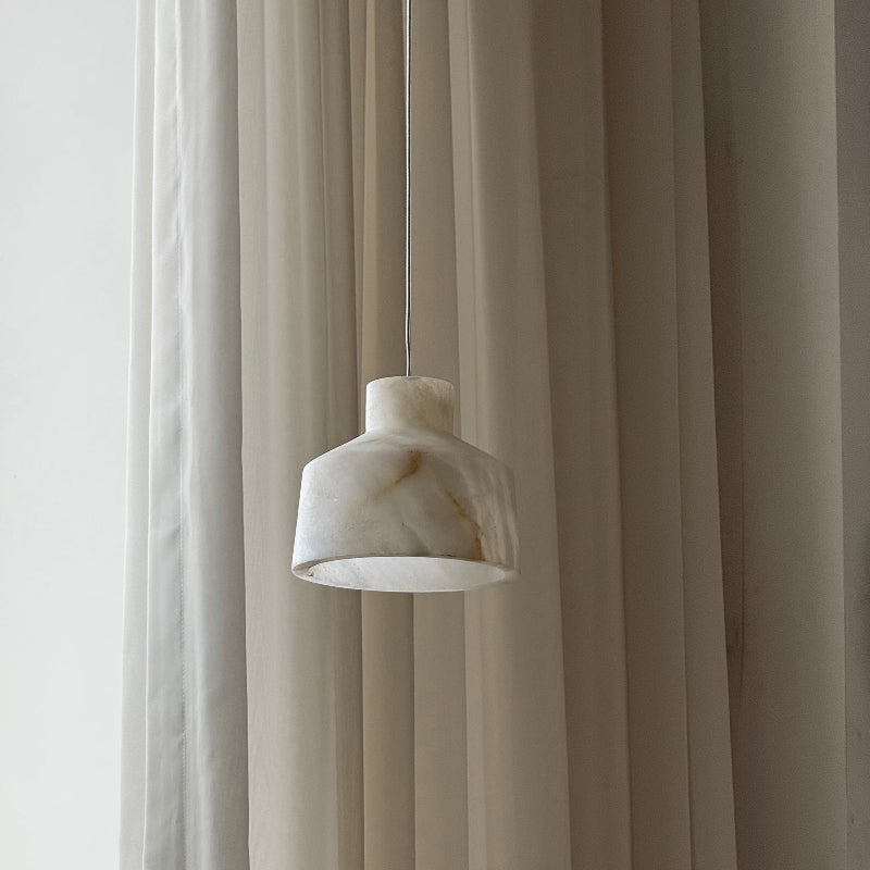 Clérachic Alabaster Pendant Light in white stone, a single drop hung against a pleated cream curtain in soft daylight.