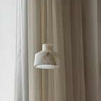 The Clérachic Alabaster Pendant Light seen side on, its white stone shade unlit and faintly veined against sheer drapes.