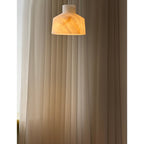 Clérachic Alabaster Pendant Light switched on, warm light travelling through the stone and washing the pleated curtain behind.
