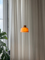 The brown stone Clérachic Alabaster Pendant Light lit at dusk, the shade glowing amber beside a tall window and a monstera.