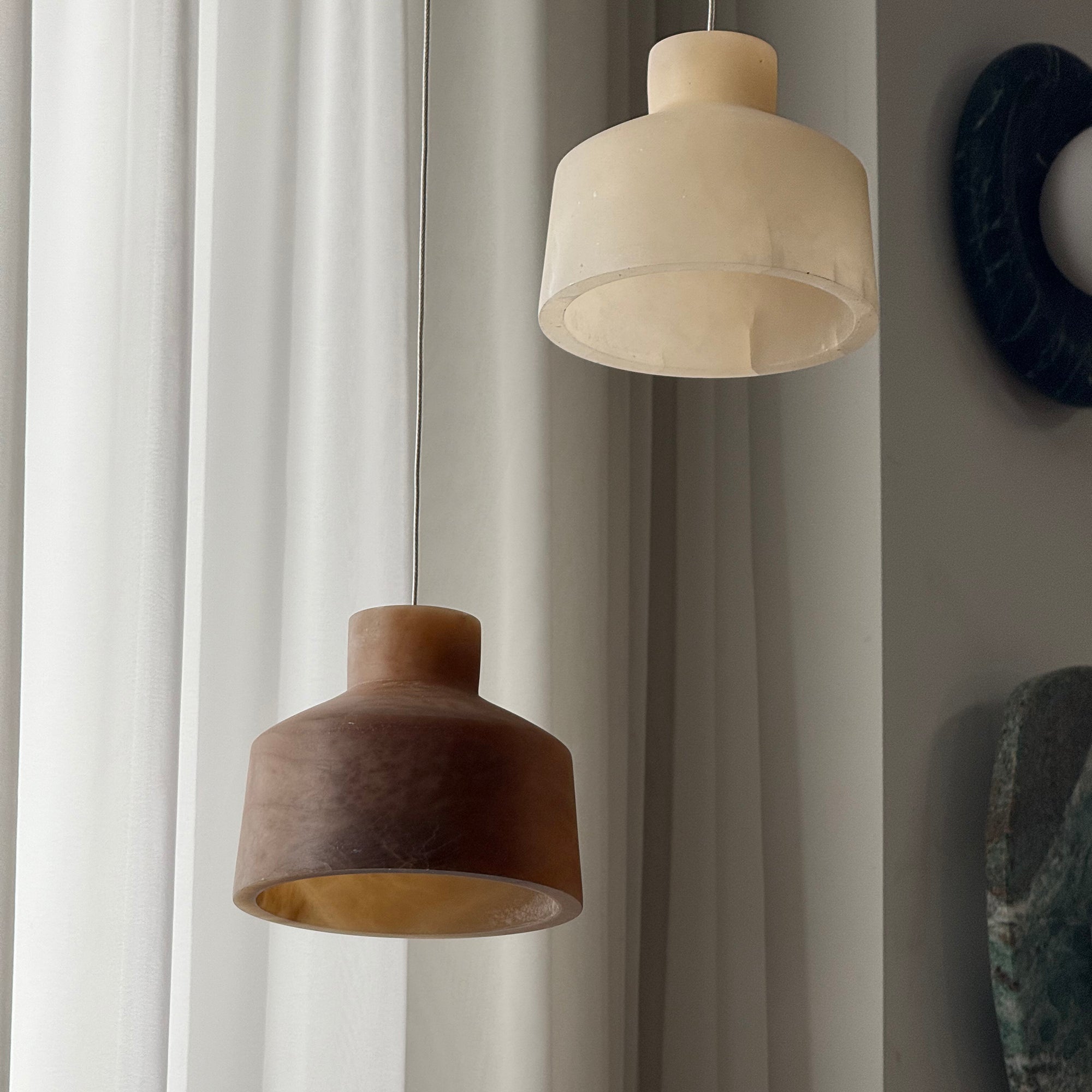 Two shades of the Clérachic Alabaster Pendant Light side by side, pale cream and deep brown, showing the hollowed stone interior.
