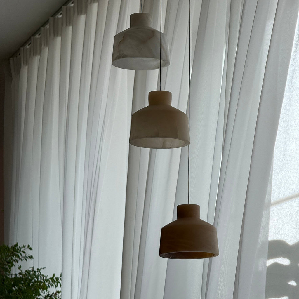 Clérachic Alabaster Pendant Light hung as a three-head cluster along a wall of white curtains, shades unlit in flat daylight.