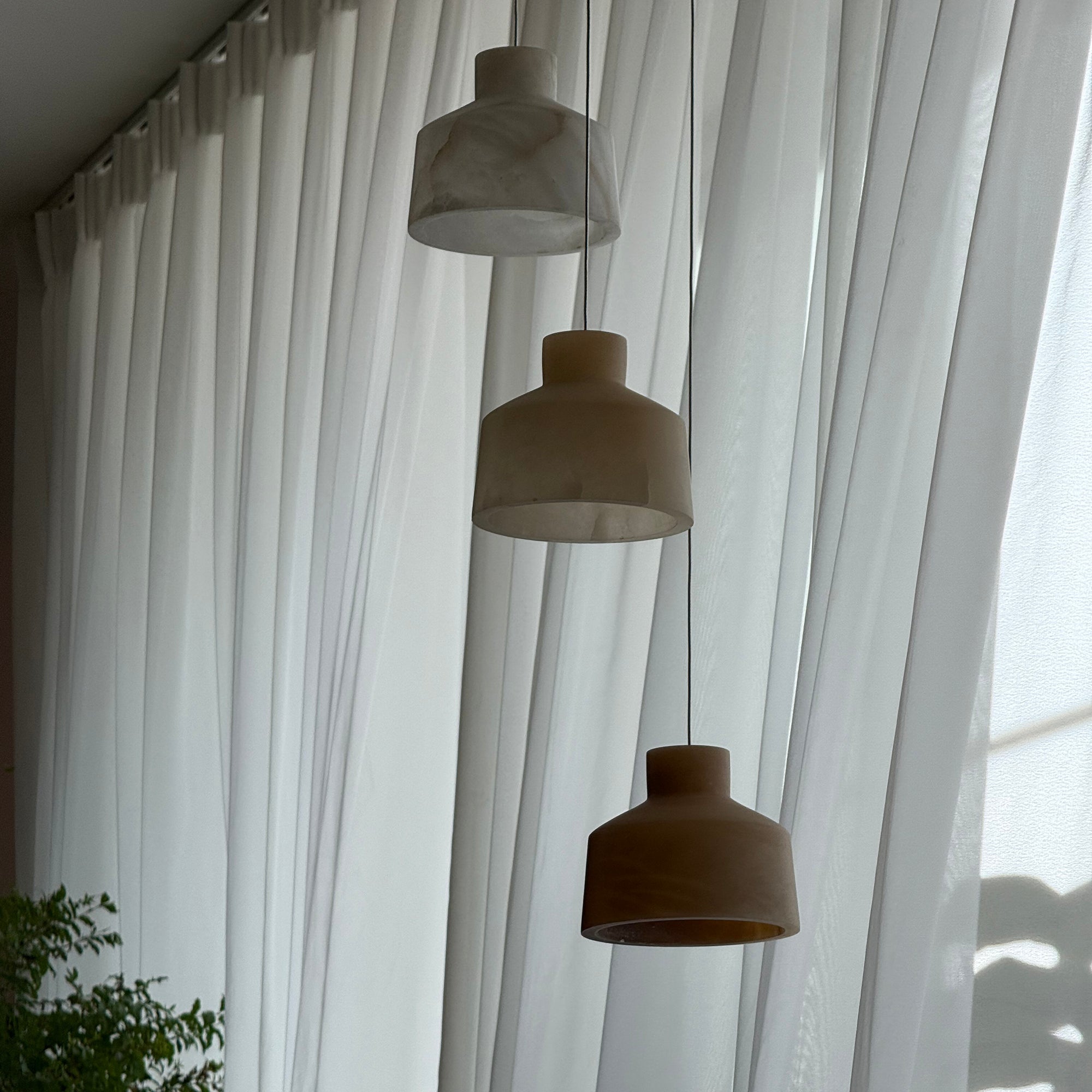 Clérachic Alabaster Pendant Light hung as a three-head cluster along a wall of white curtains, shades unlit in flat daylight.