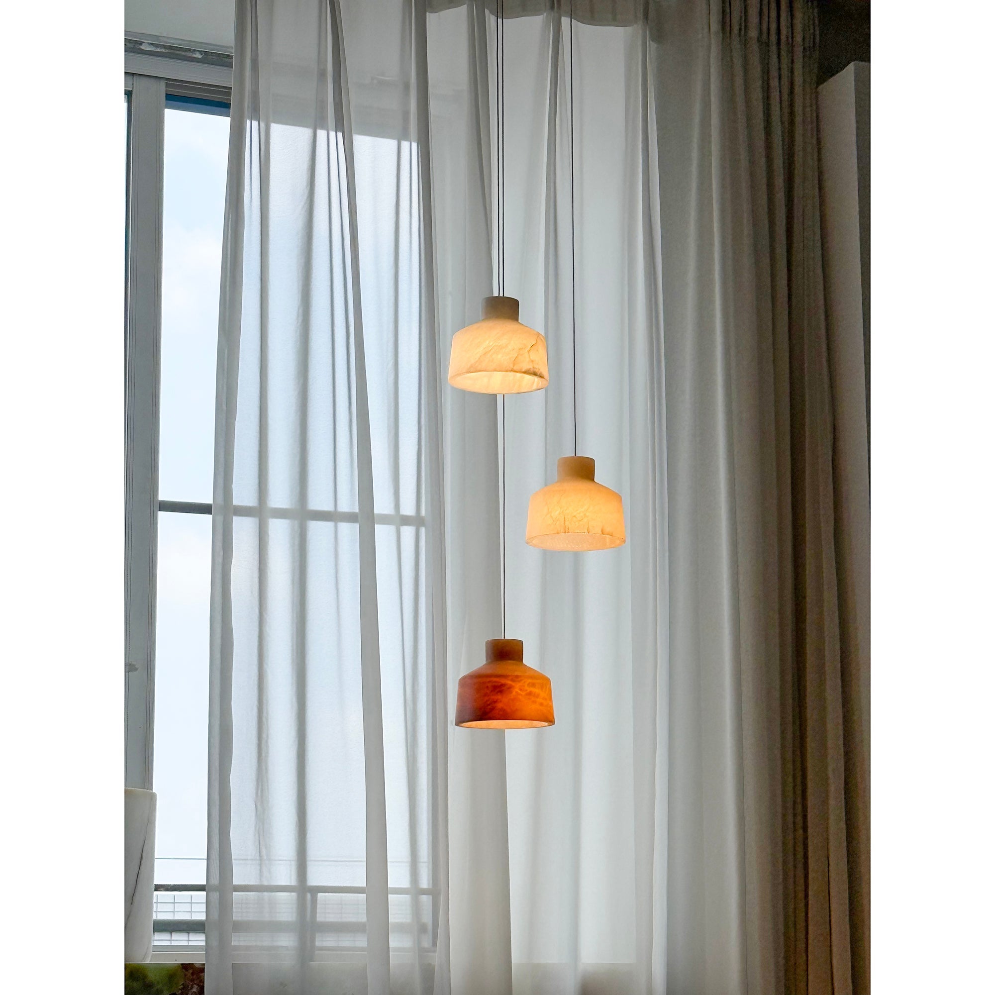 Clérachic Alabaster Pendant Light cluster lit in front of a floor-to-ceiling window, three shades falling in a staggered line.