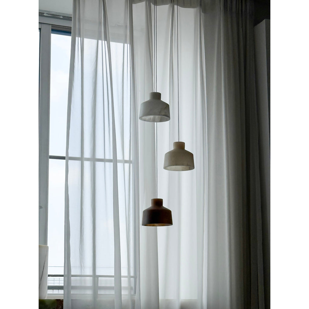Clérachic Alabaster Pendant Light cluster seen unlit in cool daylight, two pale shades above a darker brown one by the window.