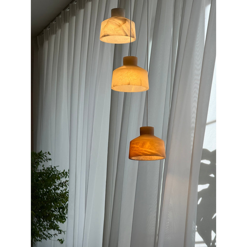 Clérachic Alabaster Pendant Light cluster viewed from below, sunlight on the curtains and the lowest shade glowing warm amber.