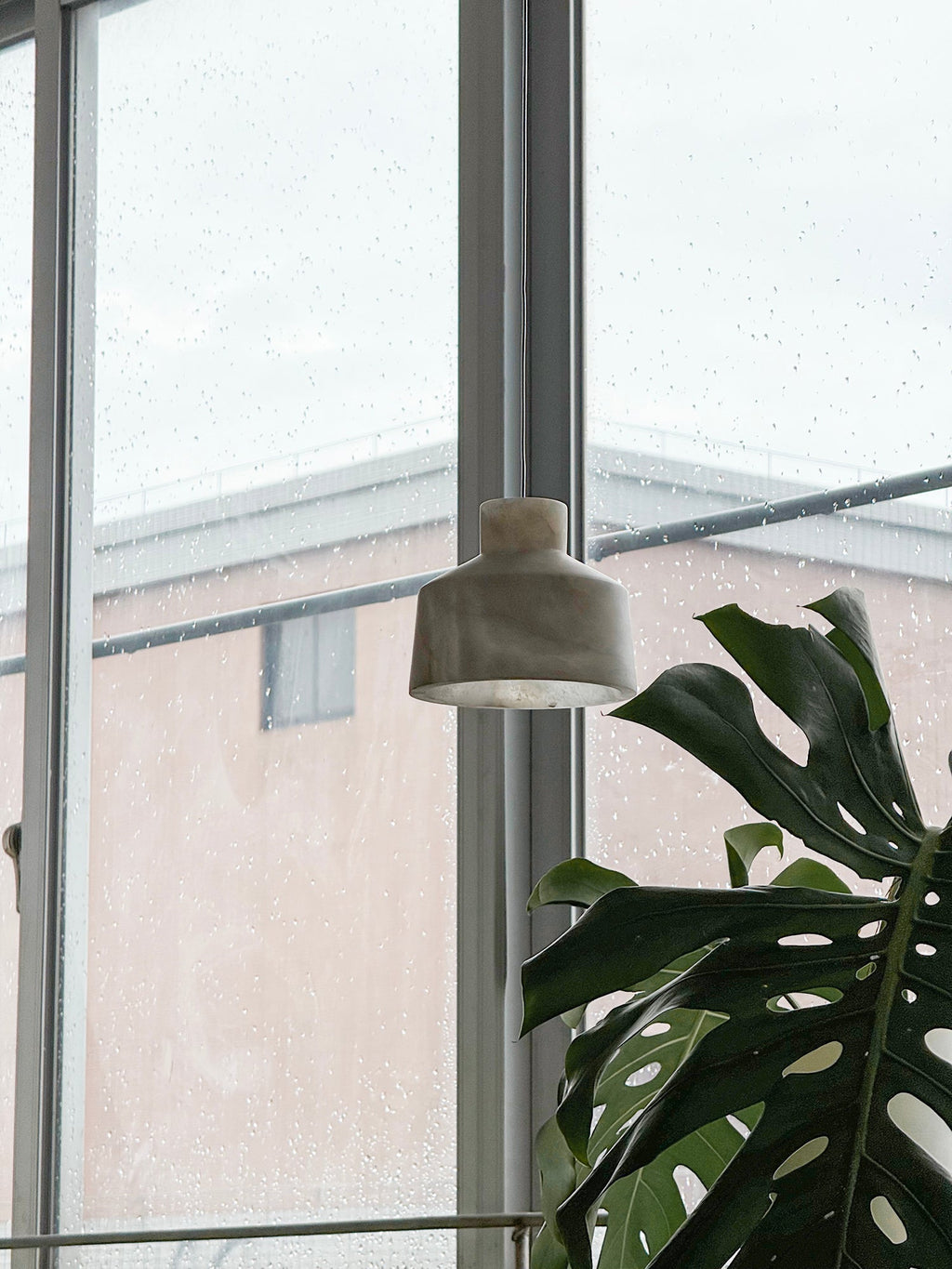 Clérachic Alabaster Pendant Light unlit at a rain-flecked window, the pale stone shade reading almost like marble in daylight.