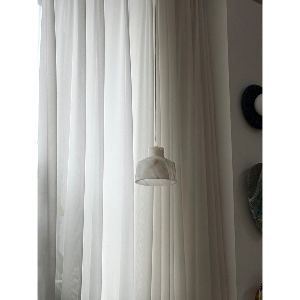 Clérachic Alabaster Pendant Light hung low on its cord against floor-length curtains, the white shade quiet in a bright room.