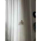 Clérachic Alabaster Pendant Light hung low on its cord against floor-length curtains, the white shade quiet in a bright room.