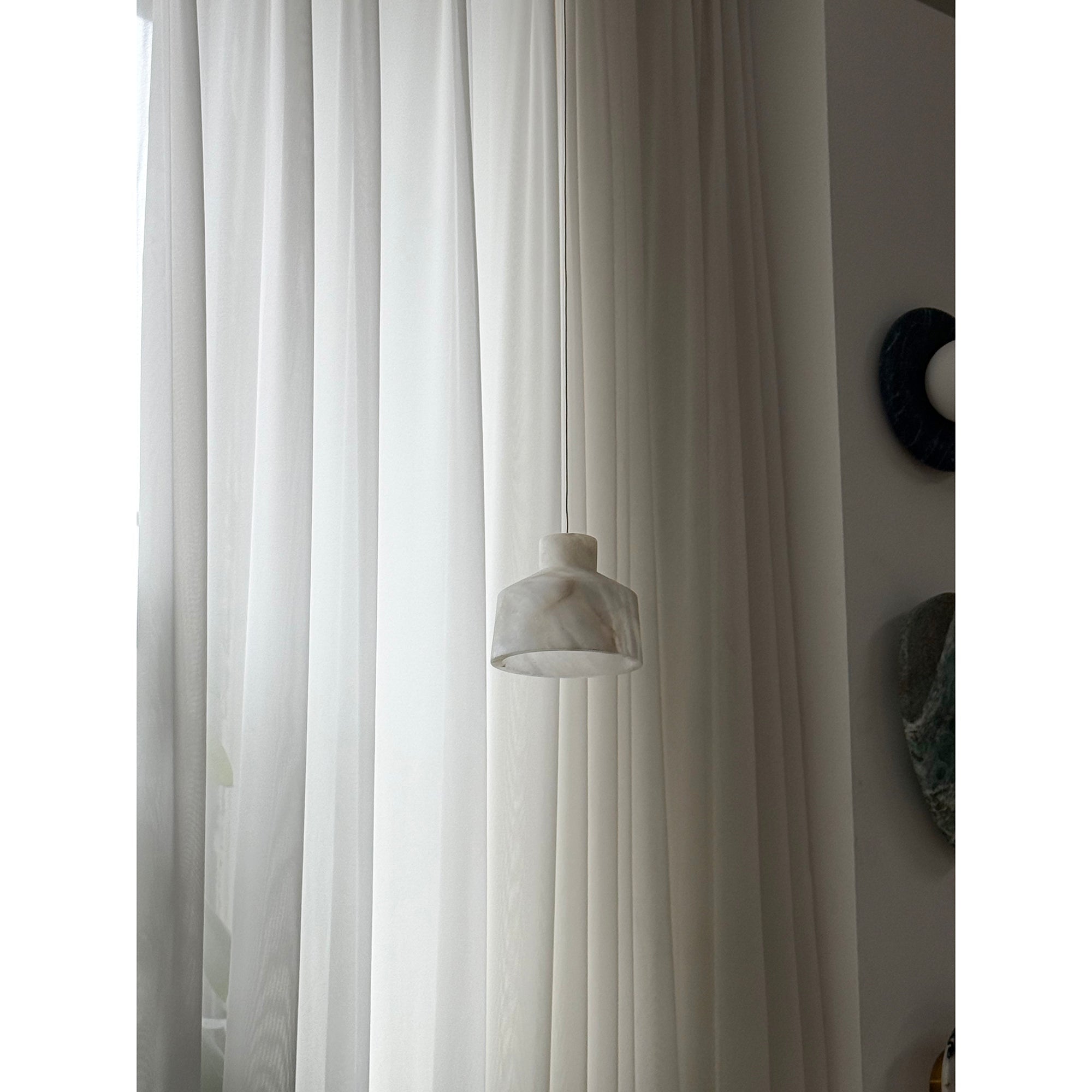 Clérachic Alabaster Pendant Light hung low on its cord against floor-length curtains, the white shade quiet in a bright room.