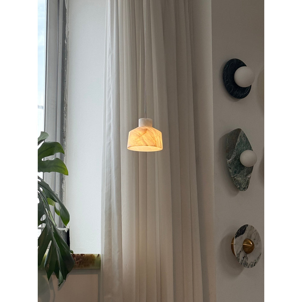 Clérachic Alabaster Pendant Light lit beside a curtained window, warm light picking out the veins in the white stone shade.
