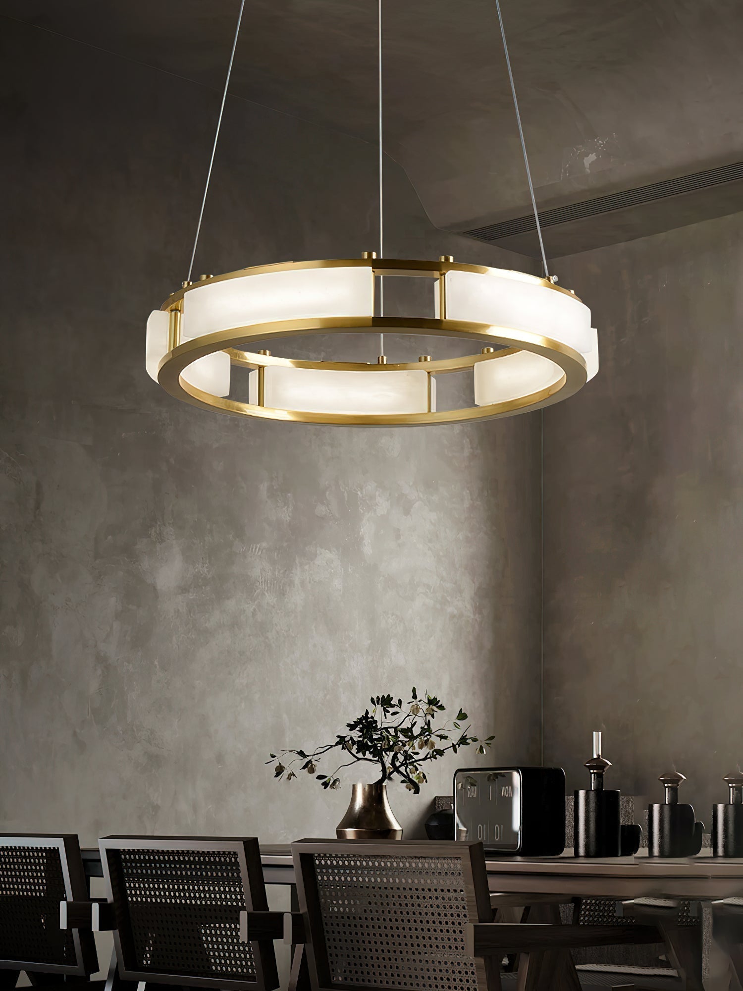 Clérachic Alabaster Ring Chandelier lighting a concrete-walled dining room above caned chairs and a long timber table.