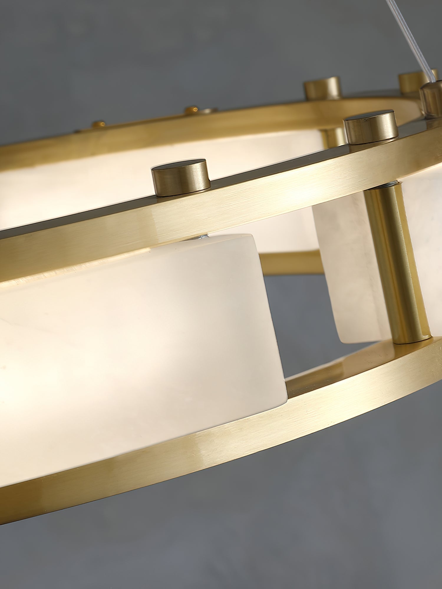 Lit Clérachic Alabaster Ring Chandelier up close, brass caps along the top rail and light glowing evenly through the stone.