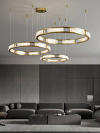 Three Clérachic Alabaster Ring Chandeliers ordered together and hung at staggered heights above a dark lounge sofa.