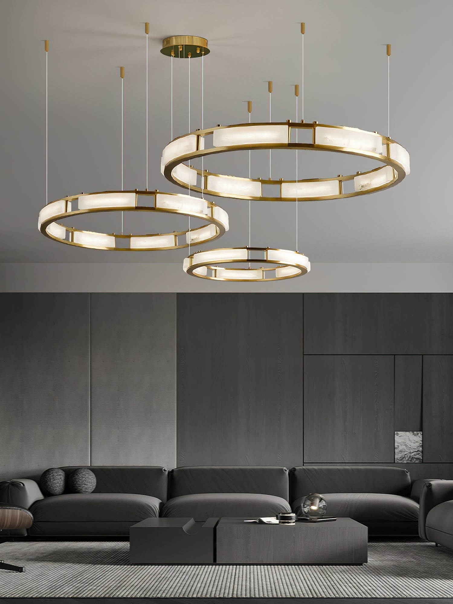 Three Clérachic Alabaster Ring Chandeliers ordered together and hung at staggered heights above a dark lounge sofa.