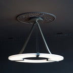 Clérachic Alabaster Ring Chandelier fitted to an ornate ceiling rose in a dark panelled room, the ring glowing softly below it.