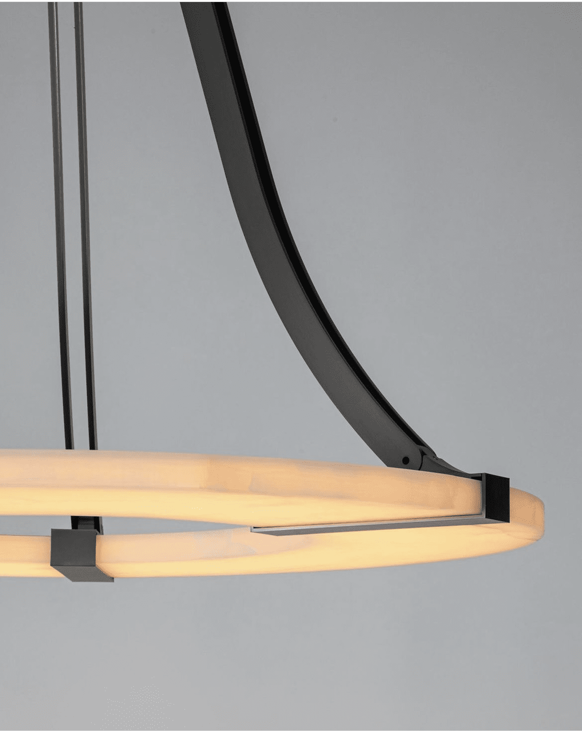 Close detail of the Clérachic Alabaster Ring Chandelier where a bronze strap clamps the glowing stone band to its curved arm.