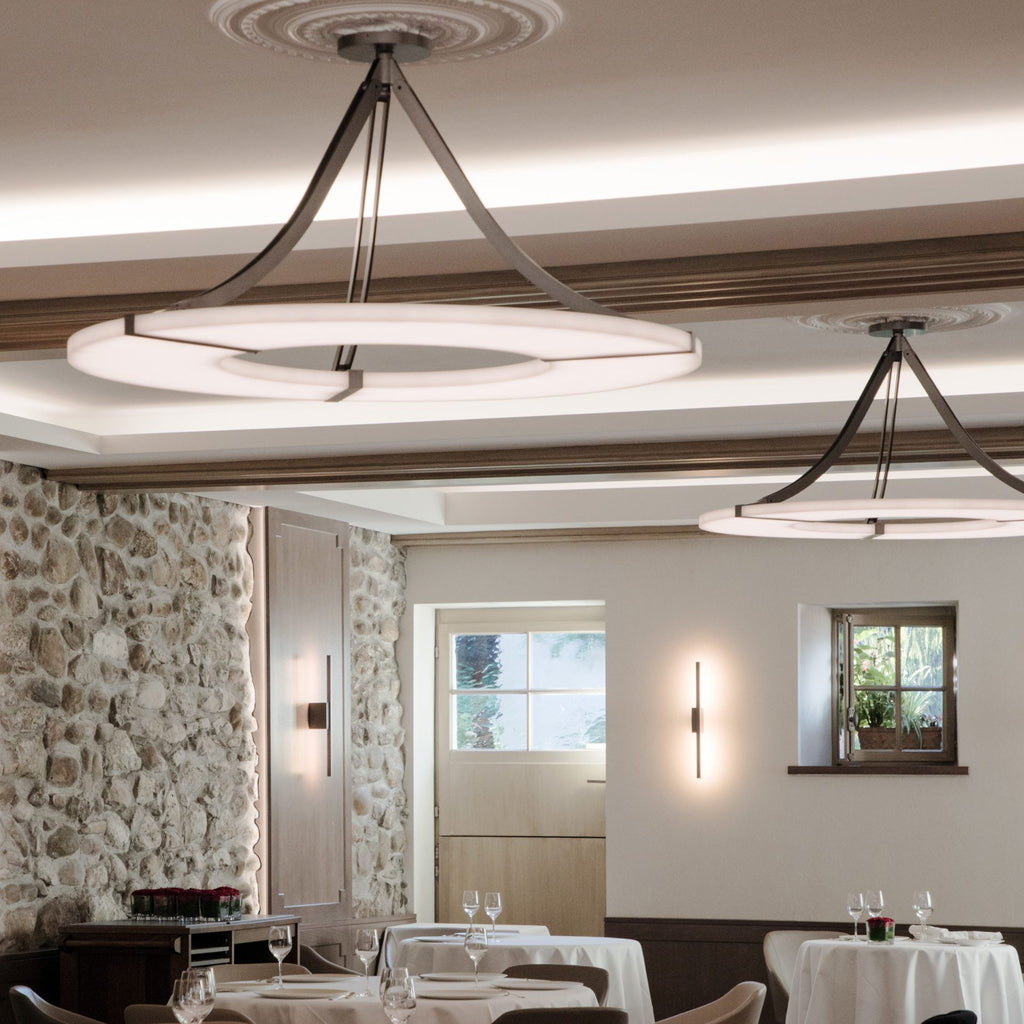 Two Clérachic Alabaster Ring Chandeliers lighting a dining room of dressed tables, stone walls and a coffered ceiling.