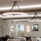Two Clérachic Alabaster Ring Chandeliers lighting a dining room of dressed tables, stone walls and a coffered ceiling.