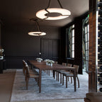 Two Clérachic Alabaster Ring Chandeliers over a long walnut table in a charcoal dining room lined with a mirrored wine wall.