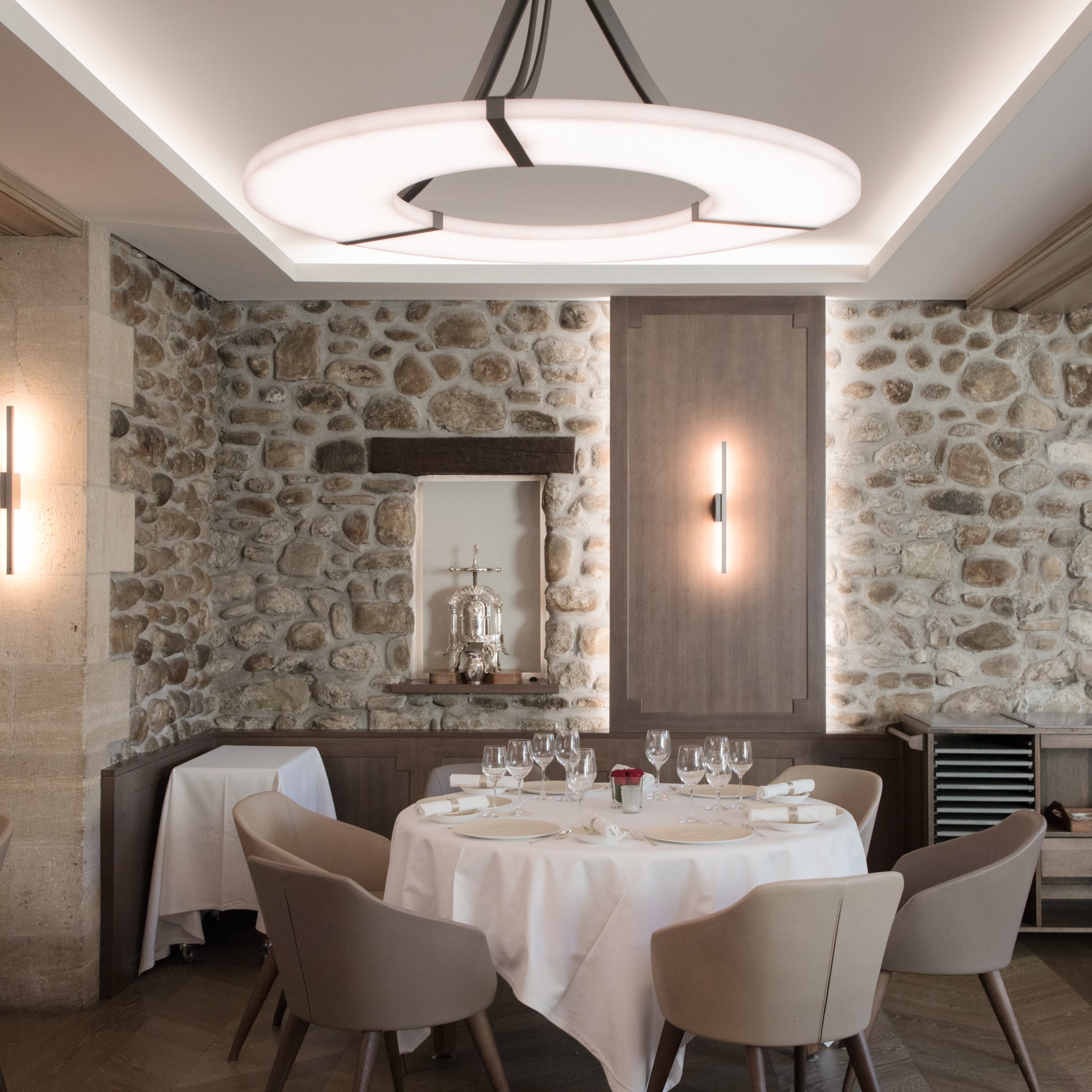 A Clérachic Alabaster Ring Chandelier centred in a coffered recess above a set round table between old stone walls.