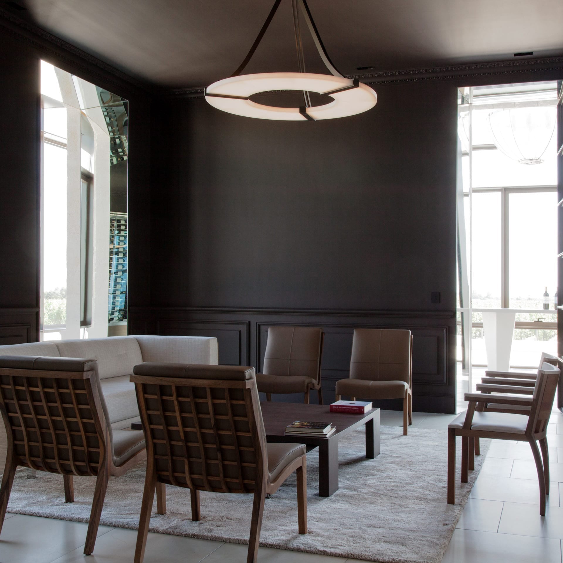 Clérachic Alabaster Ring Chandelier lighting a dark panelled lounge of leather chairs and a low table by the terrace doors.