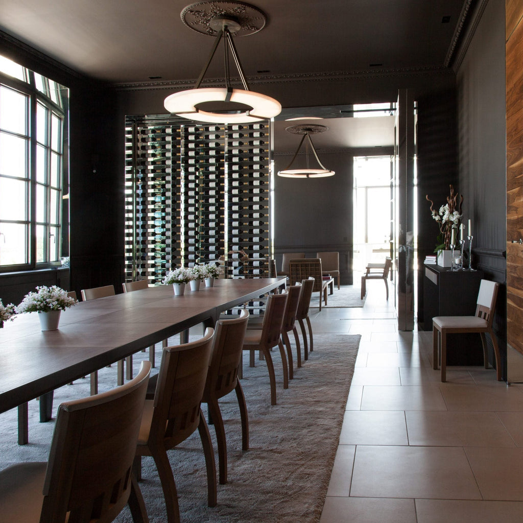 Clérachic Alabaster Ring Chandeliers running down a long dining room, glowing above the table and a mirrored rack of wine.