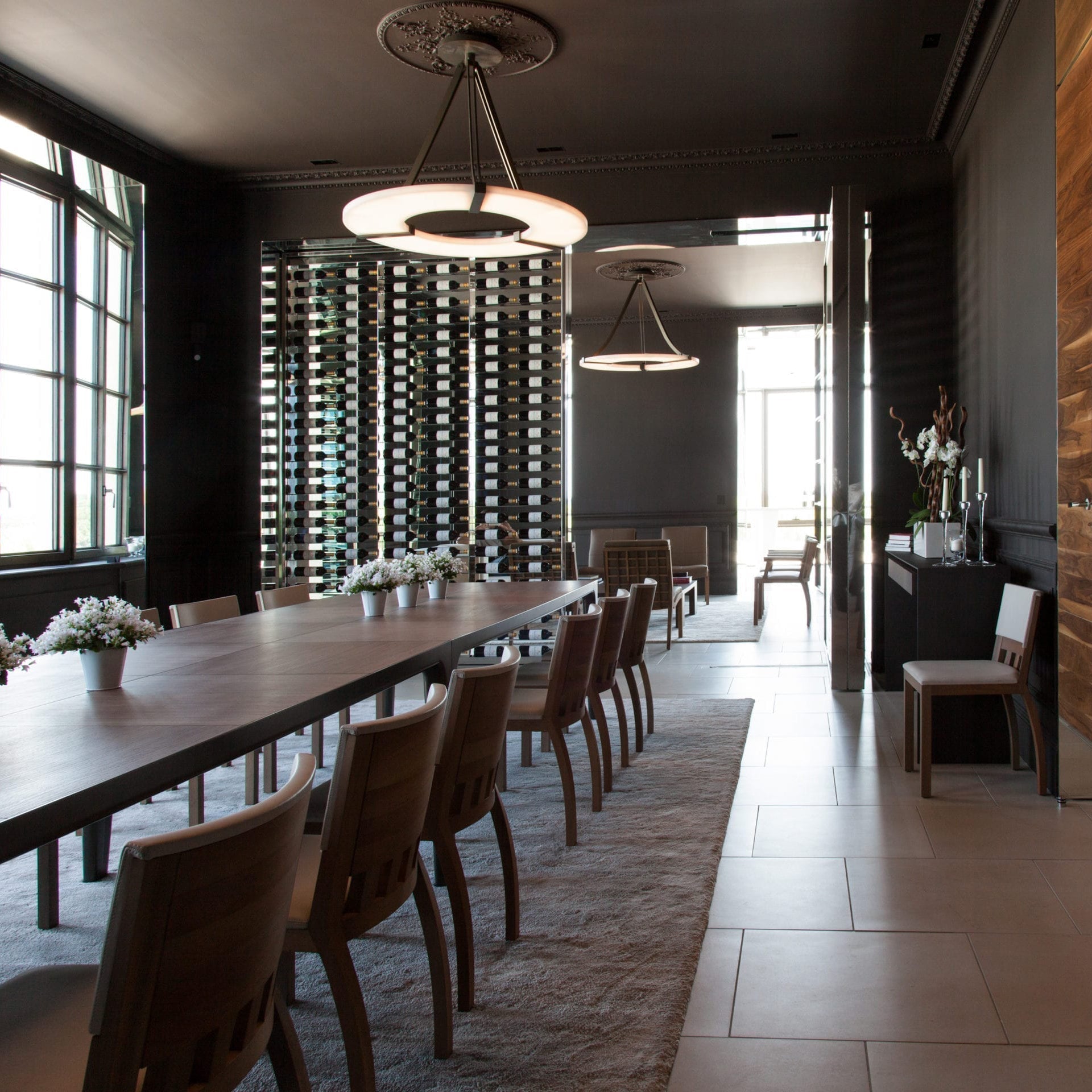 Clérachic Alabaster Ring Chandeliers running down a long dining room, glowing above the table and a mirrored rack of wine.