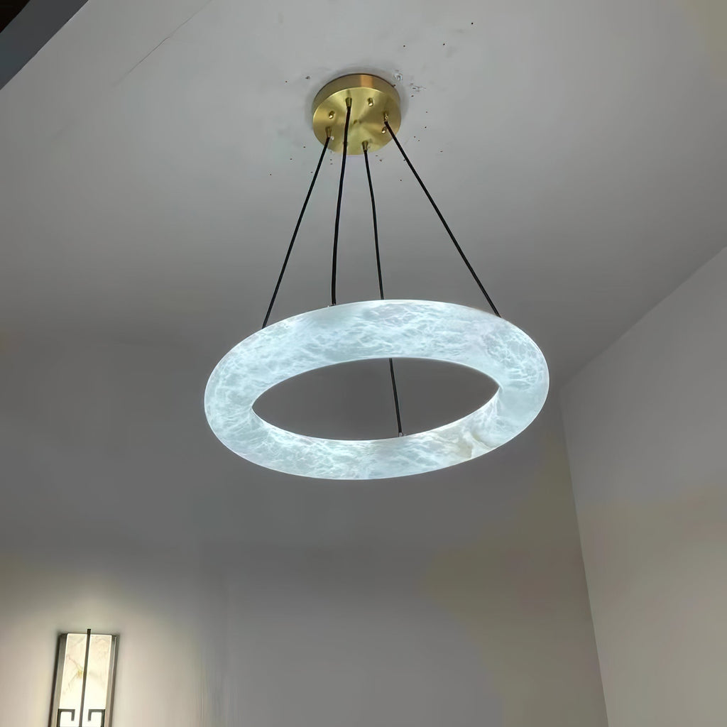 Clérachic Alabaster Ring Chandelier lit from within, the stone glowing crisp white in a hallway with a wall sconce below.