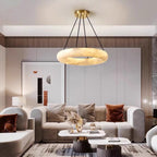 Clérachic Alabaster Ring Chandelier lit warm above a curved beige sofa and marble tables in a soft neutral living room.
