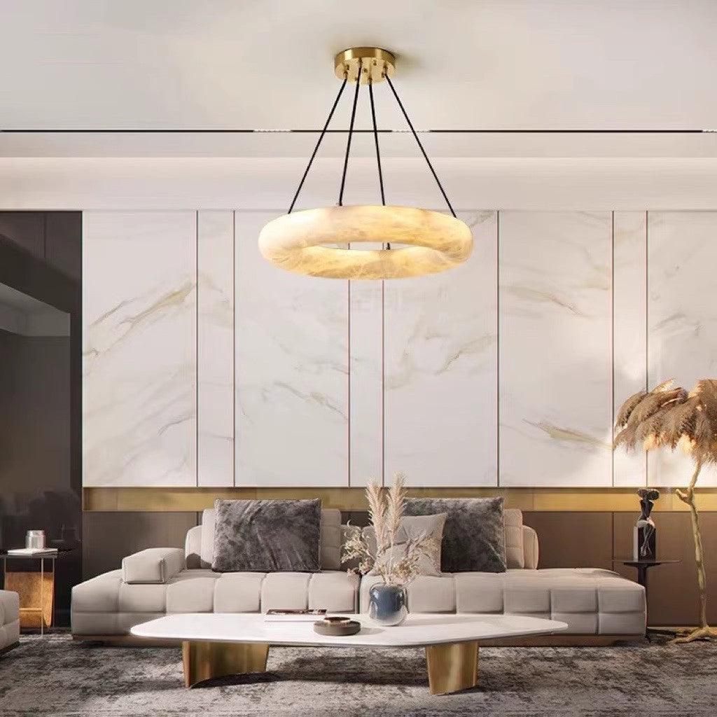 Clérachic Alabaster Ring Chandelier glowing against a marble-panelled wall above a pale sofa and a marble coffee table.