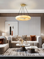 Clérachic Alabaster Ring Chandelier warm-lit above a beige sofa, framed print and pampas grass in a panelled living room.