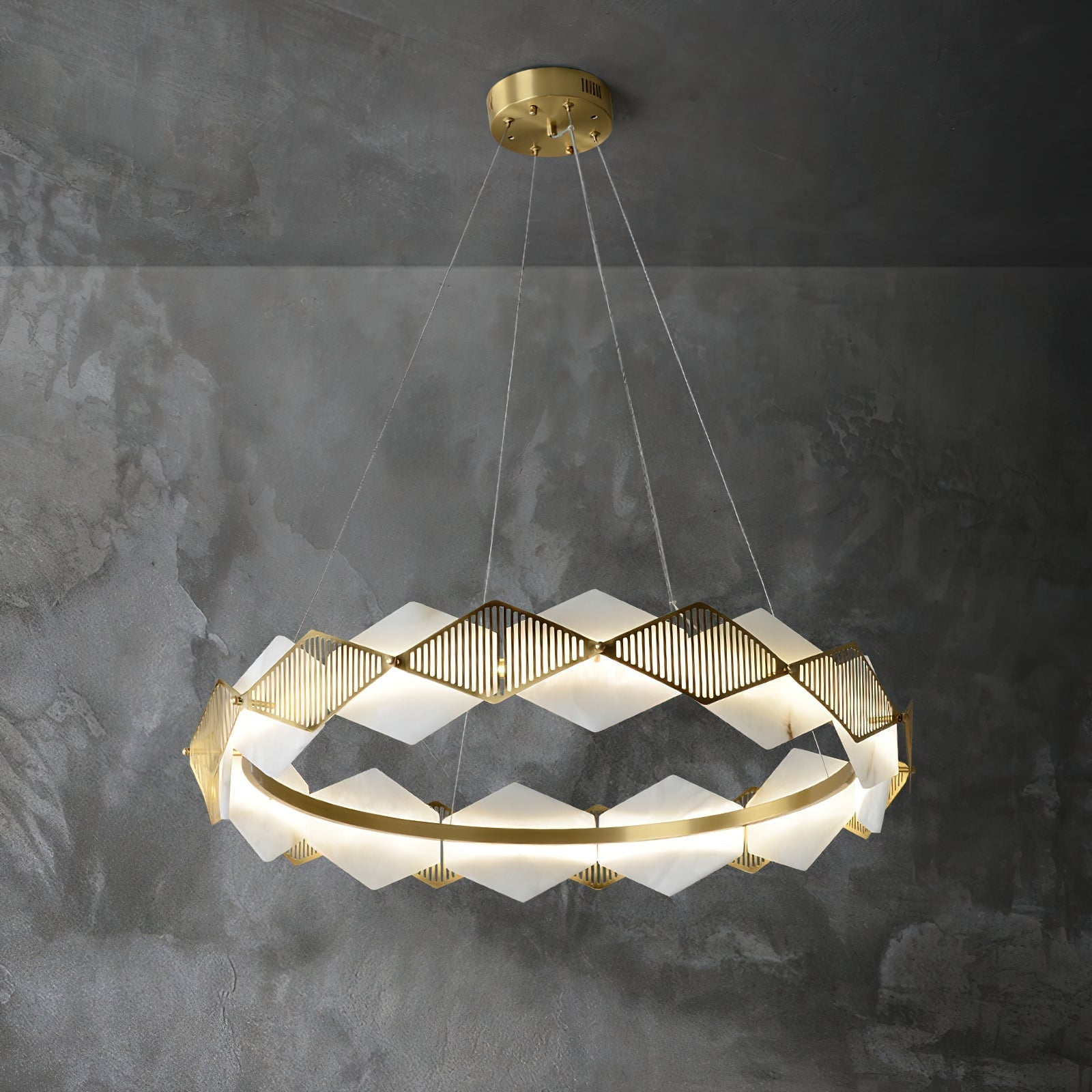 Clérachic Alabaster Ring Chandelier glowing against a dark concrete wall, the brass fins raking the light into fine lines.