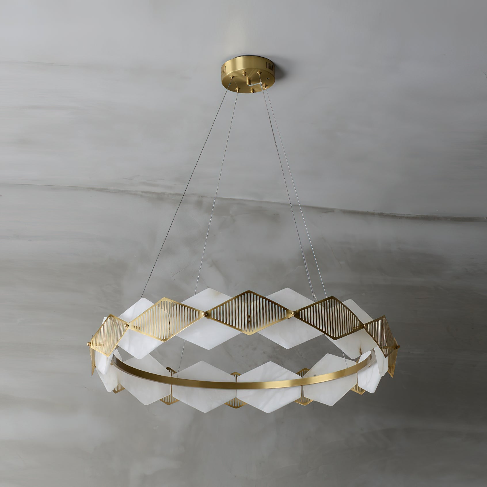Clérachic Alabaster Ring Chandelier switched off on grey plaster, chalk-white stone panels set against warm brass.