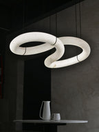 The Clérachic Alabaster Ring Chandelier lit above a dark dining corner, stone veining glowing gold over a small marble-topped table.