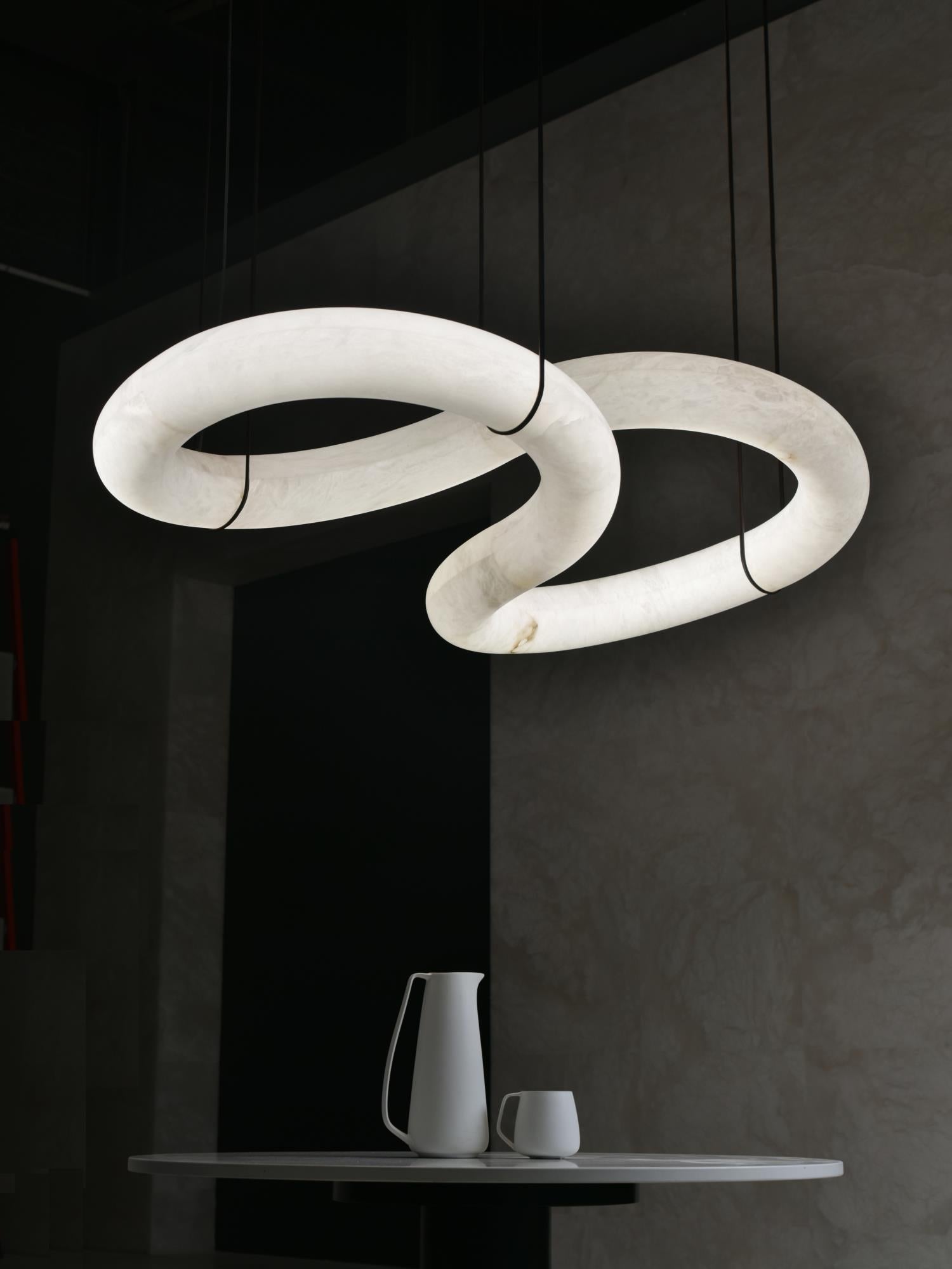The Clérachic Alabaster Ring Chandelier lit above a dark dining corner, stone veining glowing gold over a small marble-topped table.
