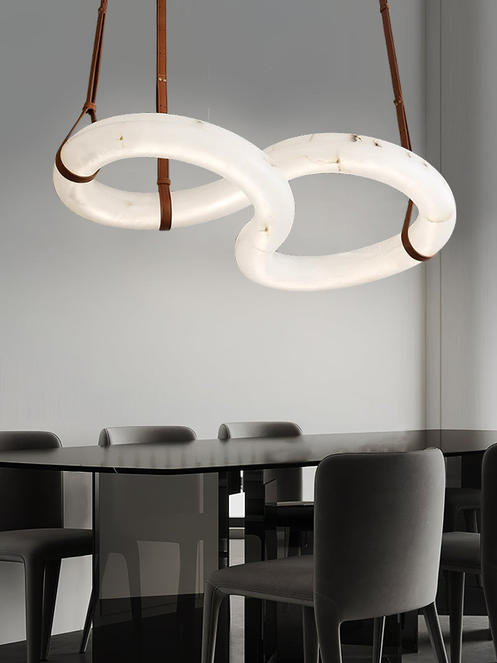Clérachic Alabaster Ring Chandelier suspended above a black glass dining table, grey chairs and a plain pale wall behind.