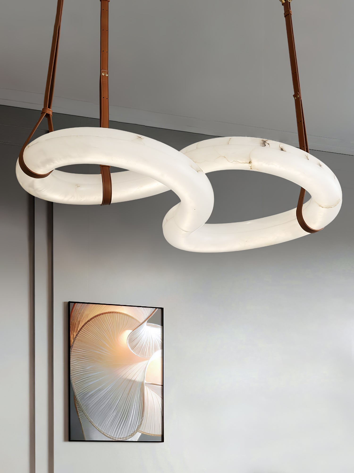 Low view of the Clérachic Alabaster Ring Chandelier, tan leather straps rising to the ceiling above a framed print.