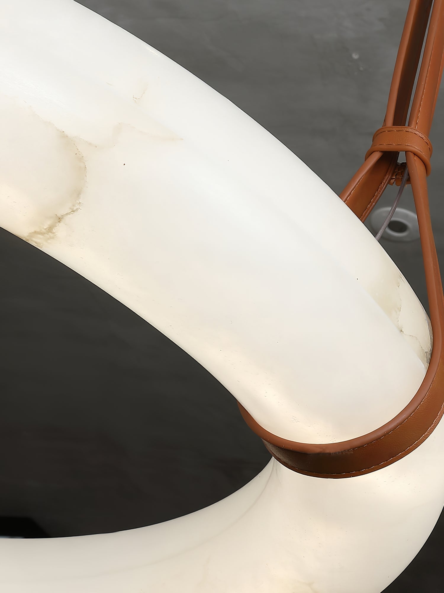 Detail of the Clérachic Alabaster Ring Chandelier, a stitched tan leather strap looped under the lit alabaster ring.