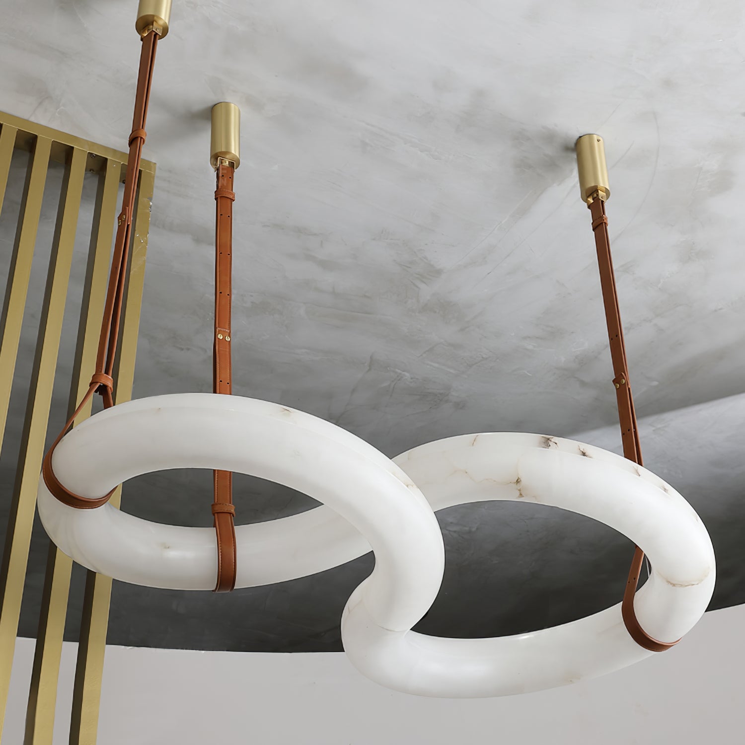 Clérachic Alabaster Ring Chandelier seen from below in a concrete-ceilinged loft, brass canopies and long tan straps in view.