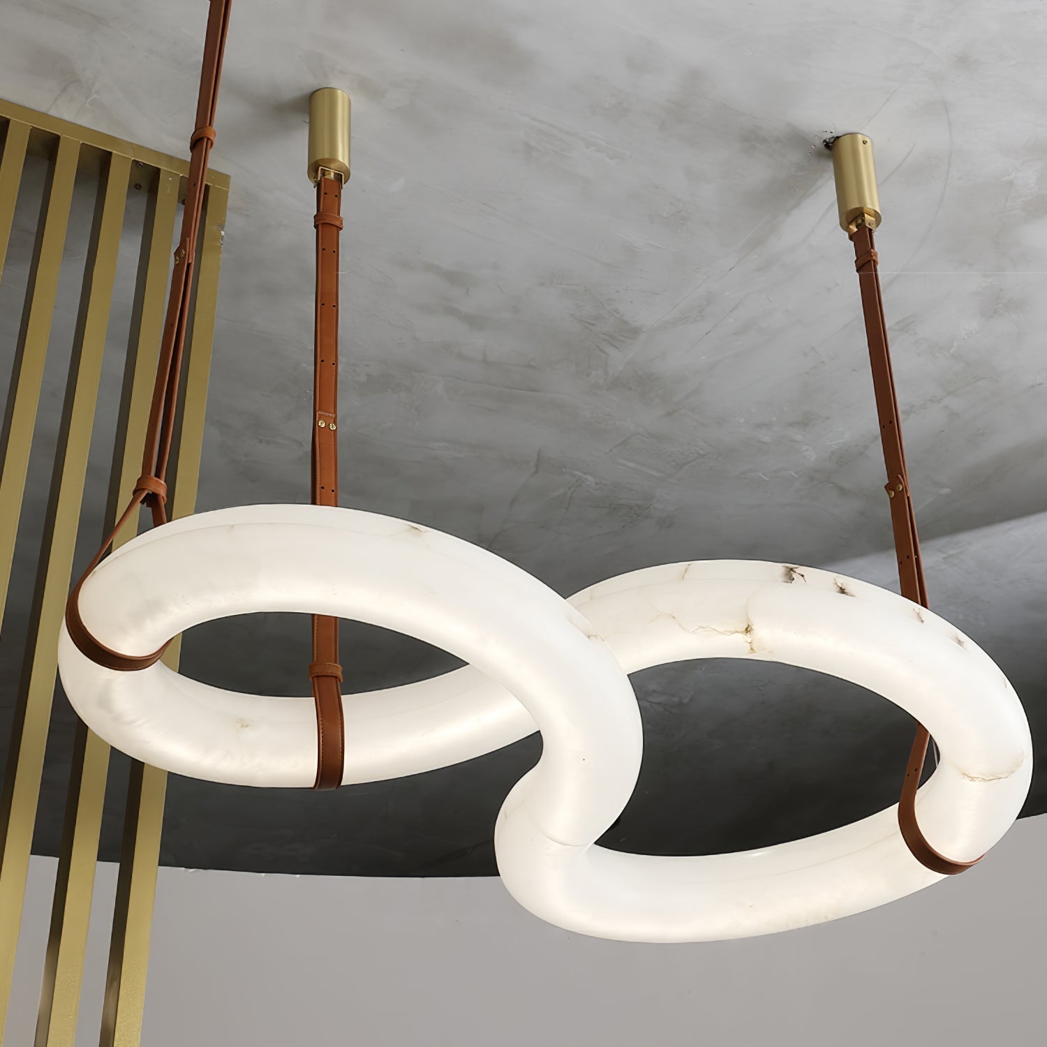 Wide angle on the Clérachic Alabaster Ring Chandelier in a concrete loft, the linked rings hanging beside a brass screen.