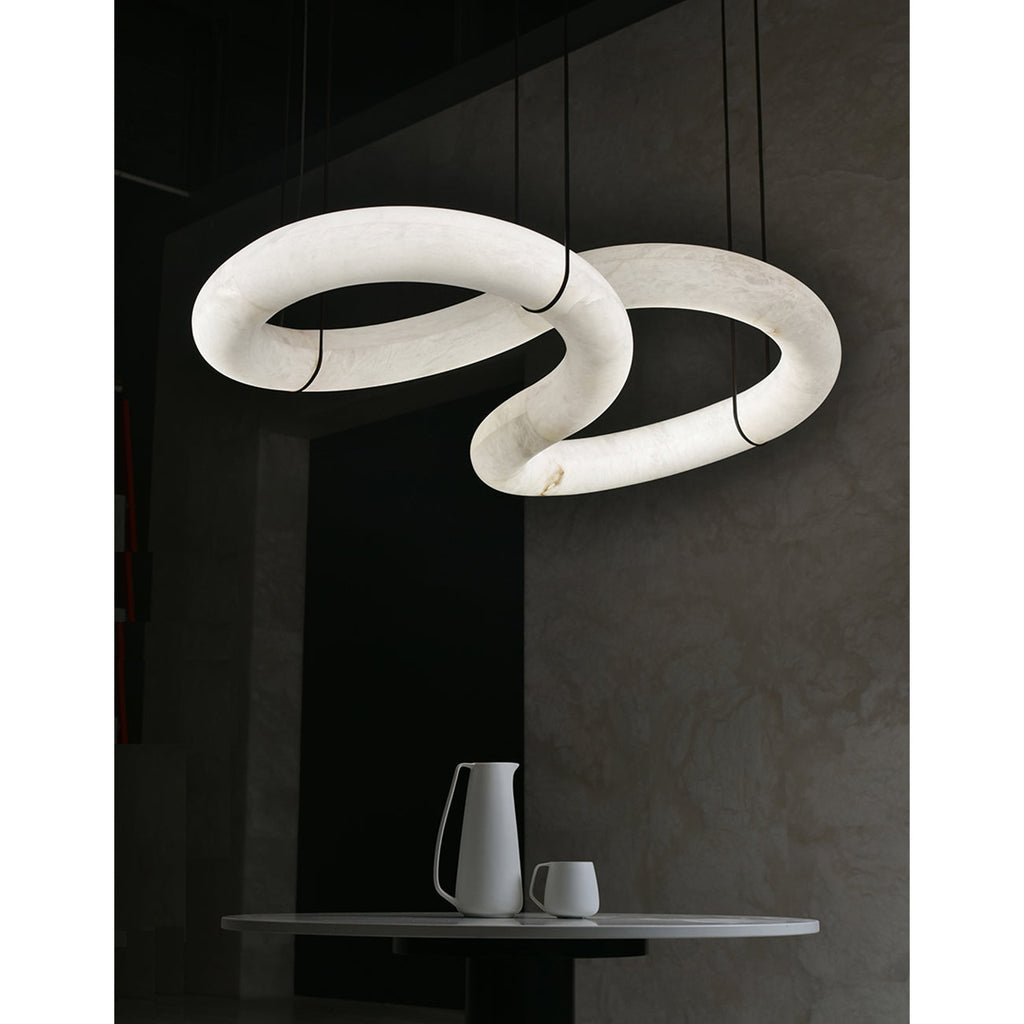 Two loops of the Clérachic alabaster ring chandelier glowing from within in a dark, stone-walled dining corner.
