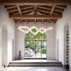 A long Clérachic alabaster ring chandelier lit under exposed timber trusses in a white brick entrance hall.