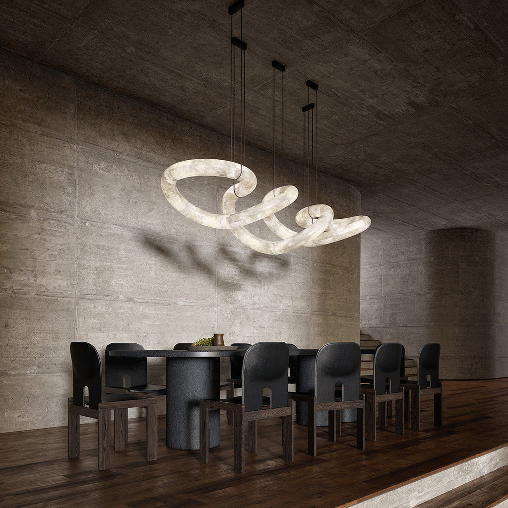 The Clérachic alabaster ring chandelier lit over a long dark dining table, casting soft shadows on a concrete wall.
