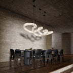 The Clérachic alabaster ring chandelier lit over a long dark dining table, casting soft shadows on a concrete wall.