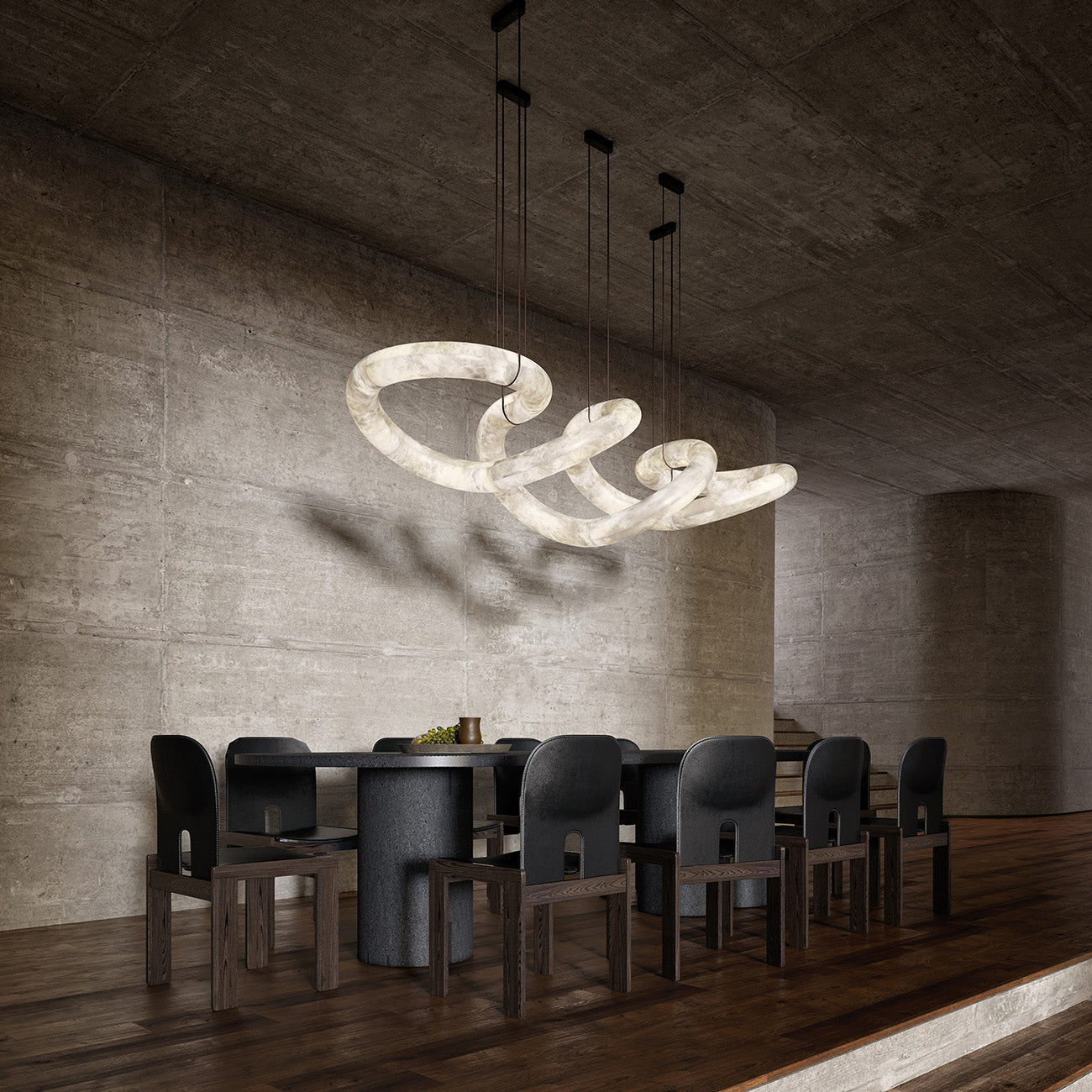 The Clérachic alabaster ring chandelier lit over a long dark dining table, casting soft shadows on a concrete wall.