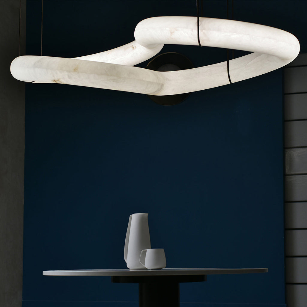 Close-up of the Clérachic alabaster ring chandelier's linked stone loops against a deep navy wall above a round table.