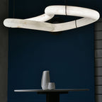 Close-up of the Clérachic alabaster ring chandelier's linked stone loops against a deep navy wall above a round table.